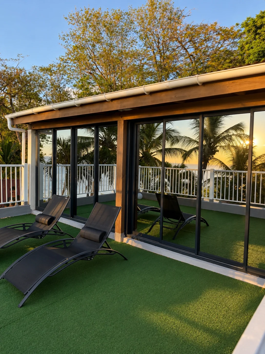 Terrasse avec transats noirs face aux baies vitrées au coucher de soleil